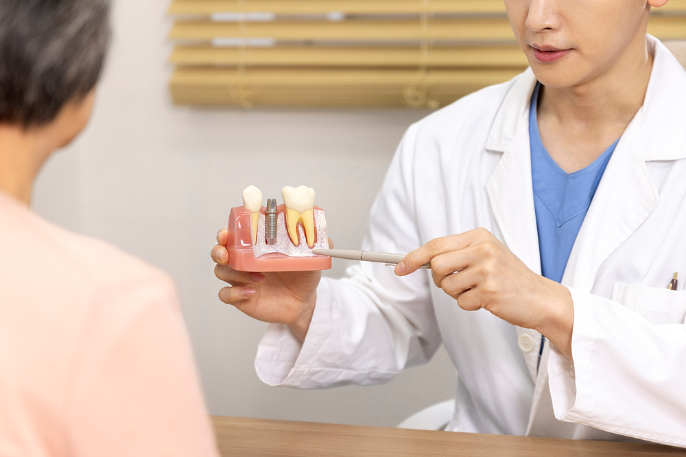 의료진이 임플란트 단면 모형으로 노년 환자에게 설명하는 상담 장면